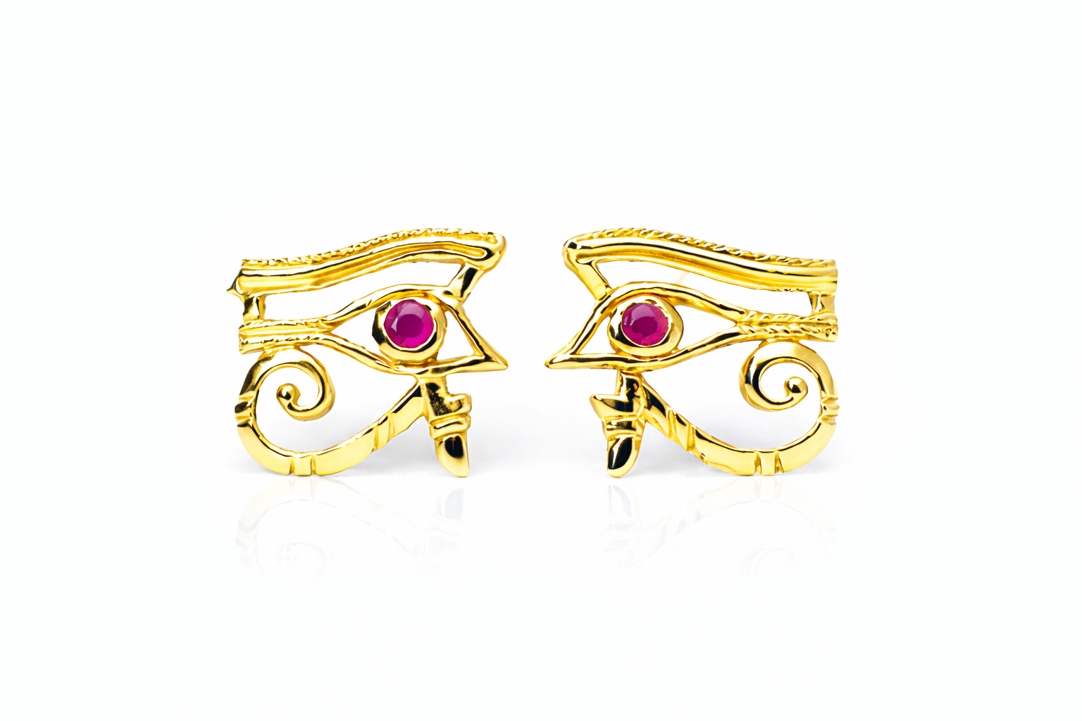 Gold eye-shaped earrings with rubies set in the eyes on a white background