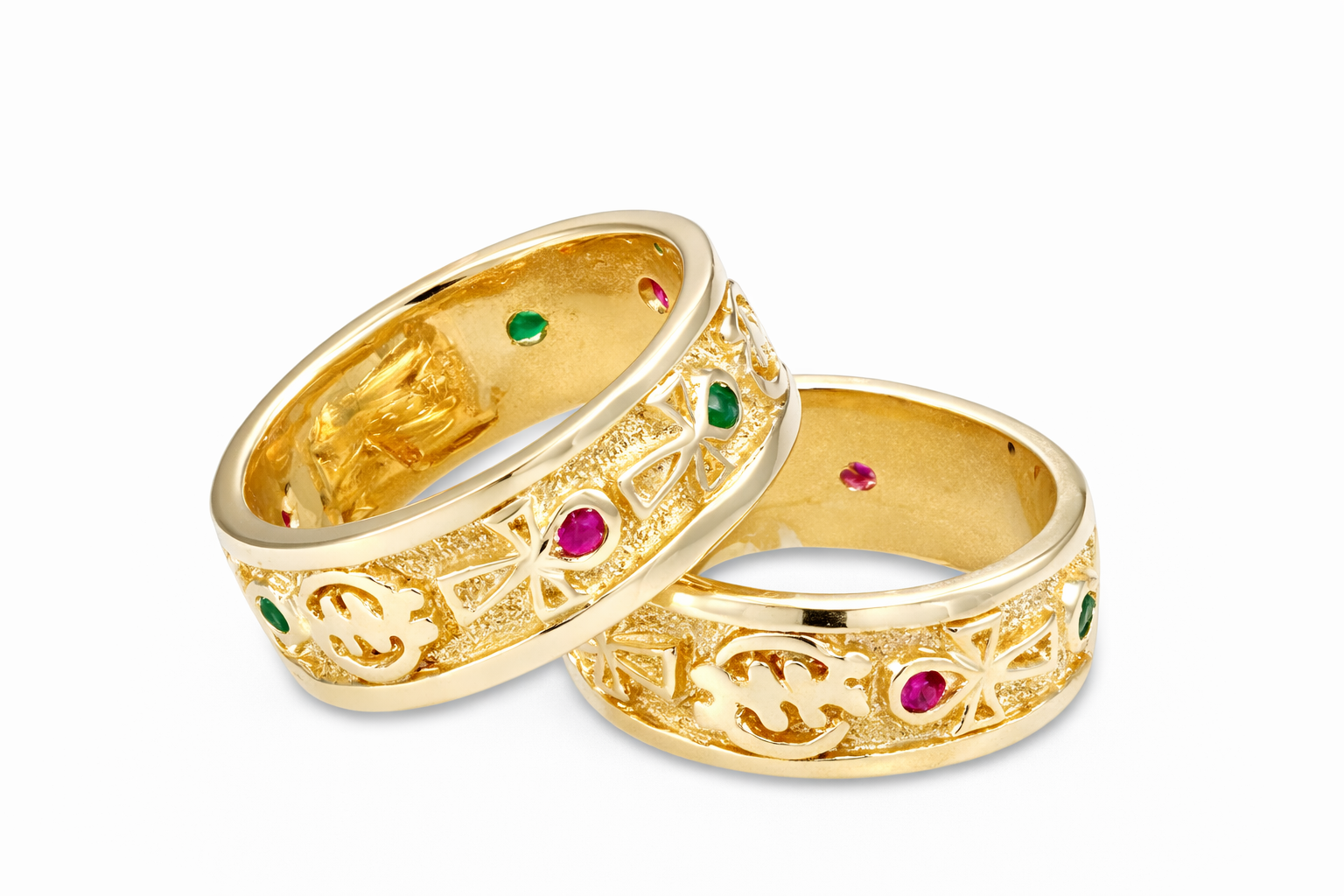 Two gold rings with gye nyame and ankh designs and colored gemstones on a white background