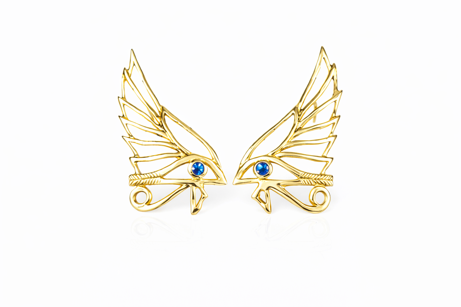 Pair of gold winged eye earrings with blue sapphires on a white background