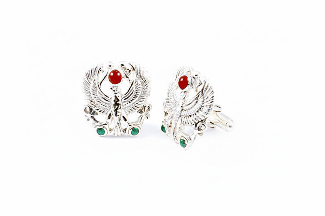 A pair of silver cuff links featuring a falcon design with red and green stones.