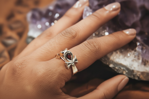 Hand wearing a 18k yellow gold ankh ring with a ruby against a textured background