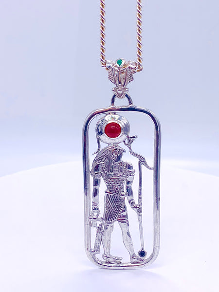 A sterling silver pendant featuring a filigree design with a figure of Heru, including Amethyst, carnelian, and emerald stones, attached to a gold-tone chain.