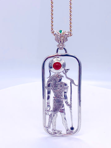 A sterling silver pendant featuring a filigree design with a figure of Heru, including Amethyst, carnelian, and emerald stones, attached to a gold-tone chain.