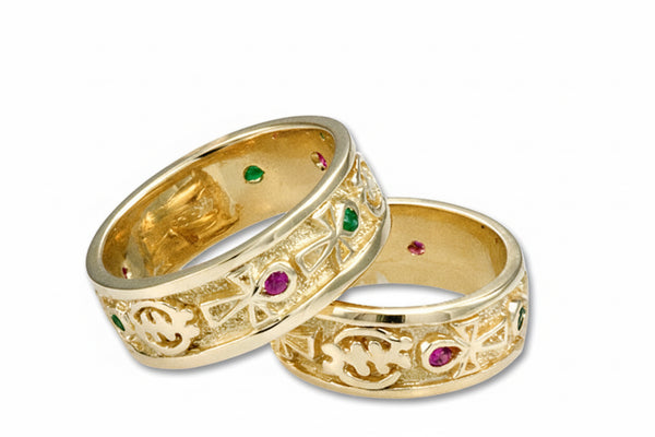 A pair of 18k yellow gold rings, one with emeralds and the other with rubies, featuring Adinkra symbols and the Kemetic Ankh symbol.