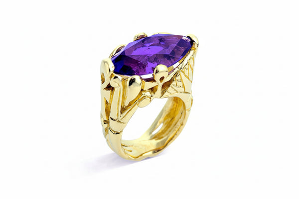 A gold cocktail ring featuring a main stone Amethyst, surrounded by four lotus flowers and two Ankhs intertwined, set in a textured gold band.