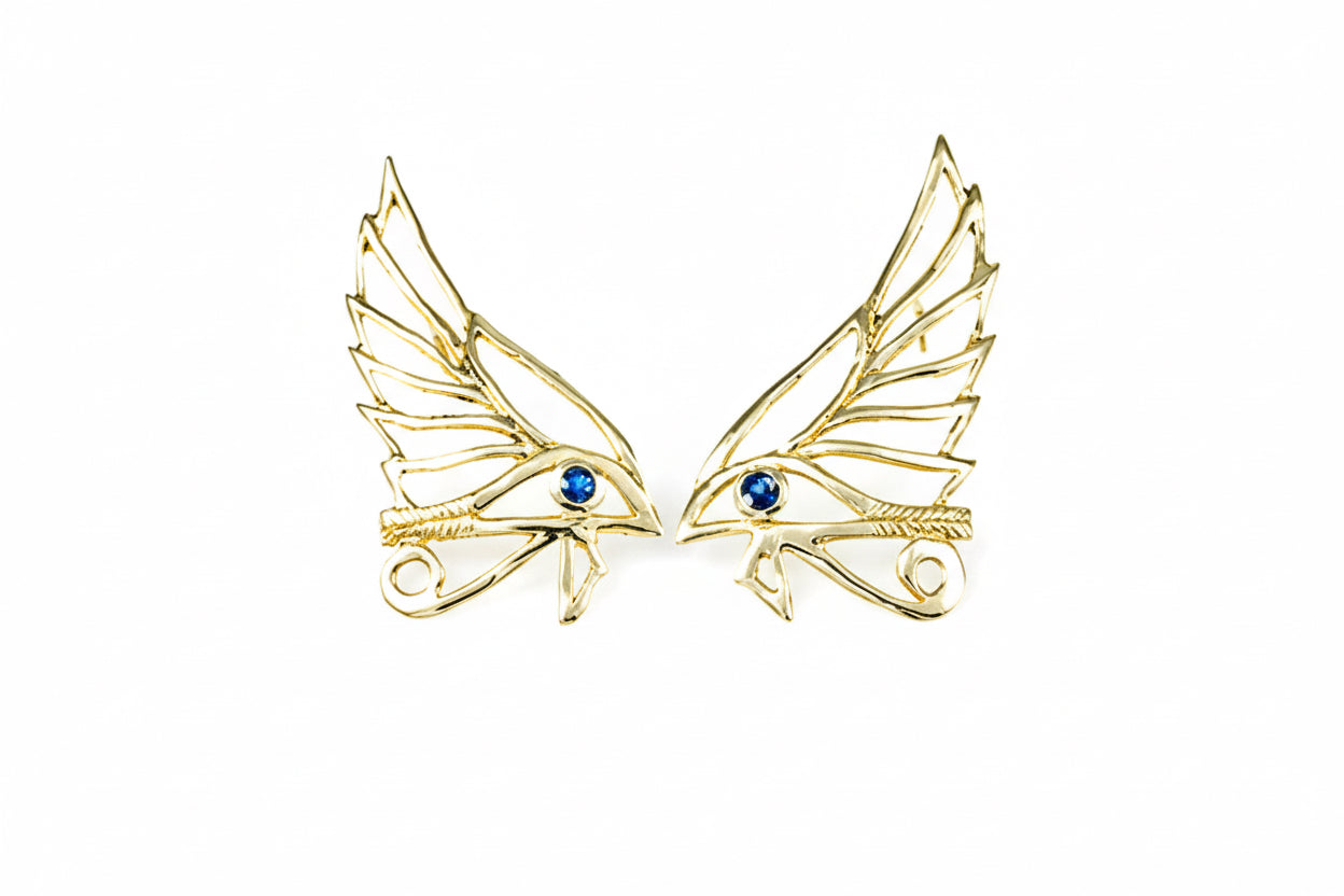 A pair of 14k yellow gold earrings with blue sapphire eyes, designed in the shape of wings.
