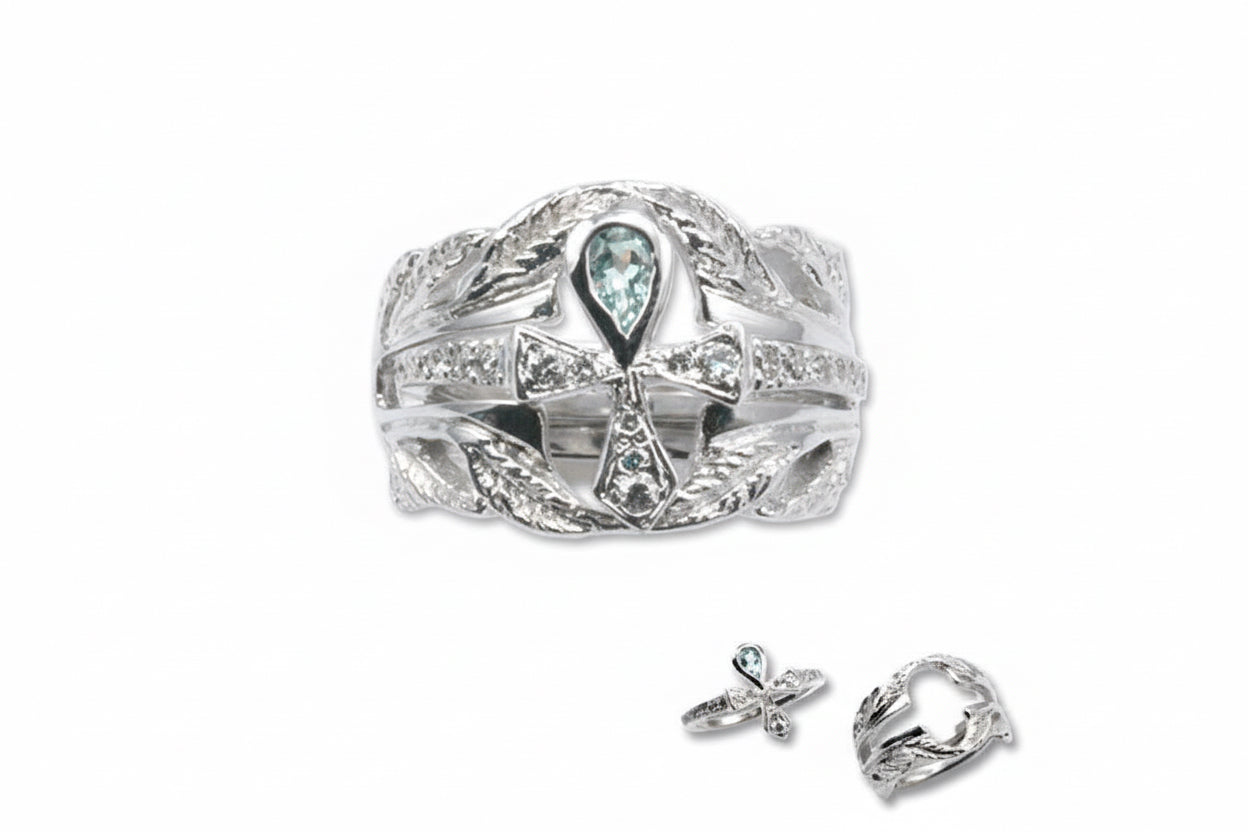 A 14k white gold engagement ring with a central aquamarine stone set within an ankh-shaped ring, surrounded by smaller white diamonds, and two smaller ring components to the side.