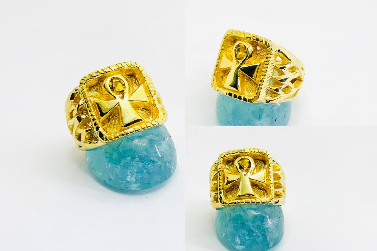A 14k yellow gold ankh ring with a citrine in the center, displayed on a white background. The ankh ring has a contoured fit and is adorned with gold filigree work.