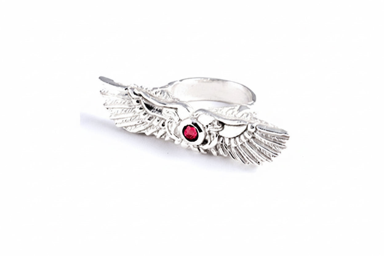 Silver ring with winged solar disc design and ruby in the center on a white background